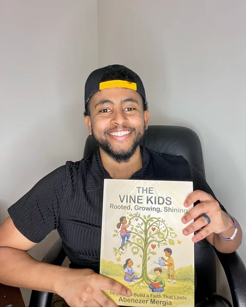 Abenezer Mergia smiling and holding a copy of The Vine Kids paperback.